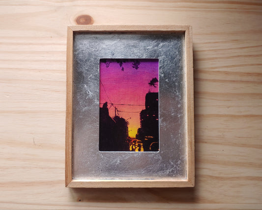 Painting on canvas in a silver and wood frame. Painting shows a purple to pink to yellow gradient sunset that silhouettes a cityscape, on the rooftops are two gargoyles. 